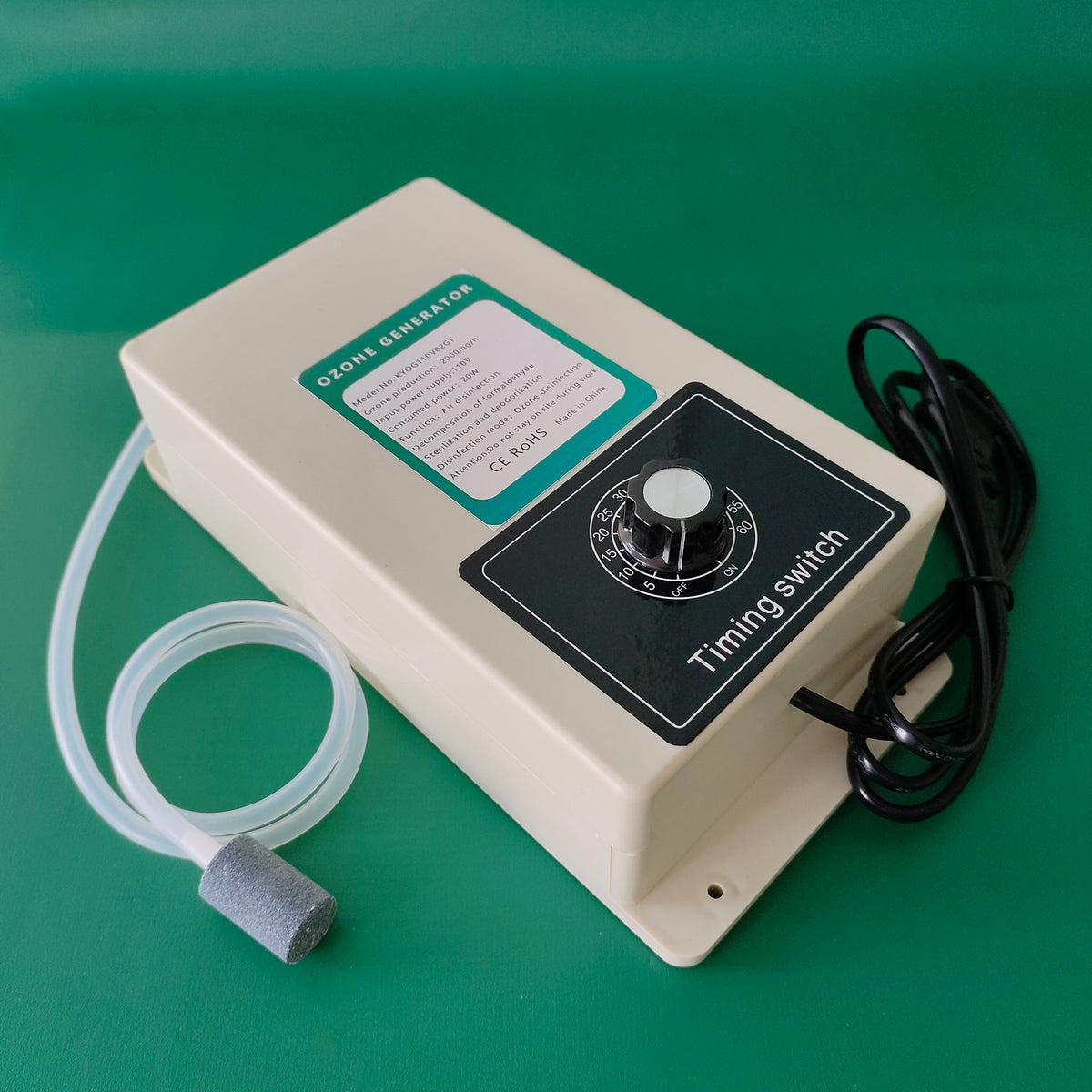 Angled high-resolution studio view of KINYO-CHINA KYOG-2GT 2000mg/h ozone generator placed on a green background displaying the rotary timing switch, CE RoHS certified specification badge, and coiled translucent silicone aeration tube with porous stone.