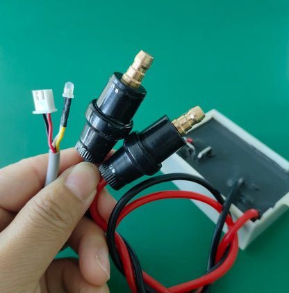    Handheld detail view of the KYOG12V03 power supply interface connectors, featuring dual black cylindrical high-voltage plug-in connectors with stepped brass contact pins, a white 3-pin input socket, and an integrated status LED indicator diode on the diagnostic feedback line.
   