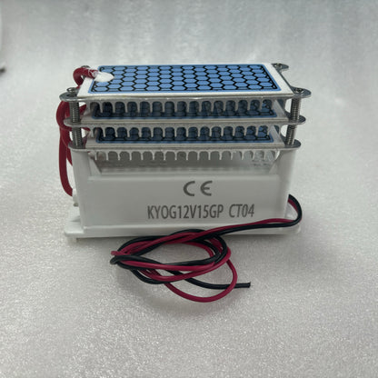   Side view photograph of the KYOG220V15GP CT04 ceramic ozone generator module on a clean white surface, showcasing the white flame-retardant housing with official CE marking and model silkscreen, red and black DC power input wires, aluminum cooling bracket, and dual honeycomb dielectric plates.
   